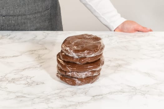 Front view of four discs of Chocolate Ginger Sugar Cookie Dough, each wrapped in plastic and stacked on a marble countertop, ready for storage or chilling.