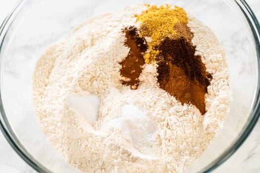 Warm spices like ground cinnamon, cloves, and ginger added to the flour in a glass bowl. These spices are key to achieving the classic gingerbread flavor in the Classic Red Gingerbread Dough.