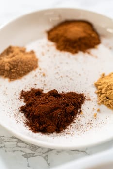 Close-up view of a plate with a blend of ground spices for Classic Gingerbread Cookie Dough, including cinnamon, ginger, cloves, and nutmeg. These spices add the warm, festive flavor typical of gingerbread.