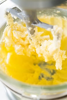 Close-up view of a mixer combining butter, sugar, and egg in the process of making Classic Sugar Cookie Dough. The partially mixed ingredients create a creamy texture as they blend together, forming the dough base.