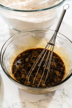 Close-up of a whisk in a bowl filled with a dark molasses mixture, a key ingredient in Classic Gingerbread Cookie Dough. The molasses adds rich color and deep flavor to this holiday favorite.