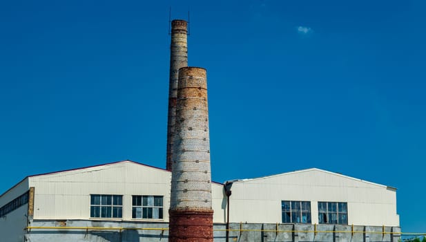 Industrial chimneys of the enterprise against the blue sky. Industrial chimney. Industrial factory building. Cloudless blue sky. Environmental protection. Ecological catastrophy.