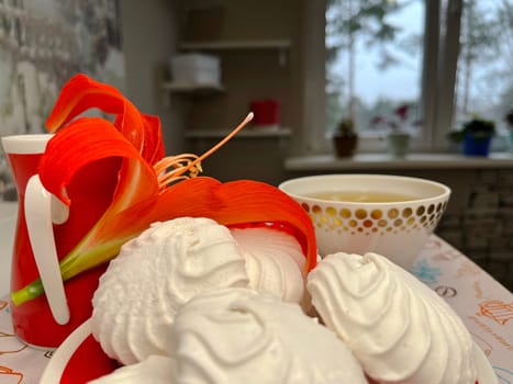 a few marshmallows on a saucer, a cup of fragrant tea and an amaryllis flower