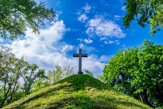 Christian cross on a mound against a blue sky with white clouds. Christian symbol. Religion and culture. Ukrainian Orthodox Church. Catholicism and Protestantism. Place of crucifixion. Easter.