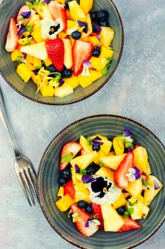 Vegan salad of pineapple, strawberries and berries, decorated with edible flowers. Top view.