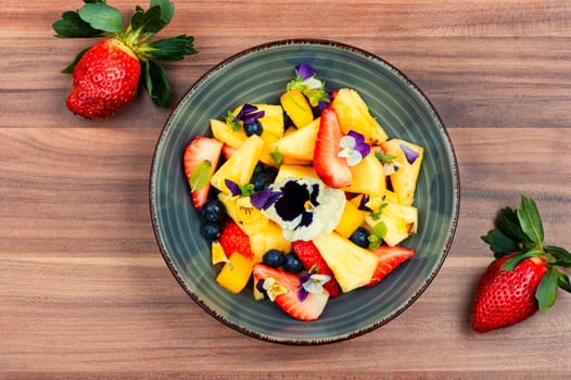 Vegan salad of pineapple, strawberries and berries, decorated with edible flowers. Top view.