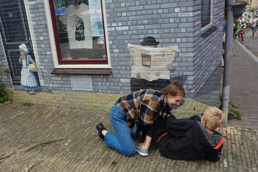 Zierikzee, Zeeland, The Netherlands , August 27th 2020 - House facade with artistic mural of a man reading the newspaper at the Plein Montmaertre in the middle of the city . Two children are lying on the floor fooling around