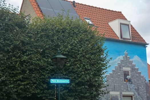 Zierikzee, Zeeland, The Netherlands , August 27th 2020 - House facade with artistic mural painting on Plein Montmaertre in the middle of the city with green hedge, lantern and street sign