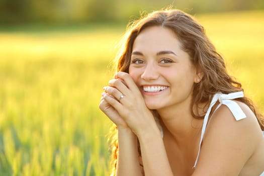 Happy woman posing in a field looking at camera at sunset