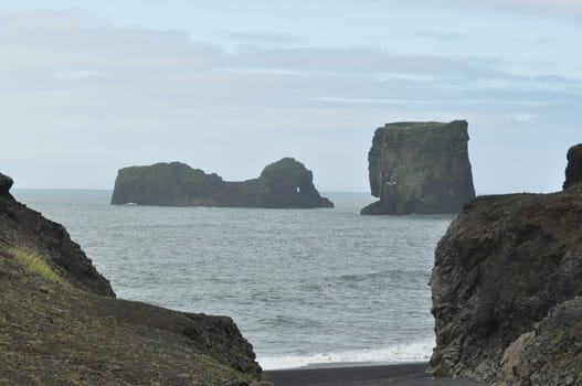 Scenic view of Icelandic coastline with waves hitting huge black rocks at overcast Dyrholaey Cape