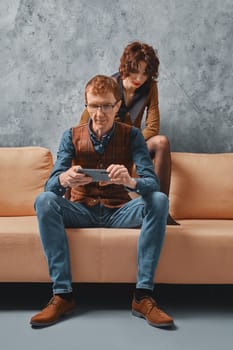 Middle aged man adjusts control of smart home on smartphone and his wife watching over him
