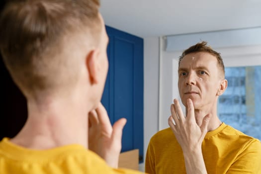 Middle-aged man applying anti-wrinkle cream. Male ageing problem.