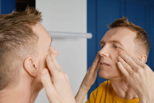 Concentrated man massaging and rubbing lotion under his eyes. Male aging problem.
