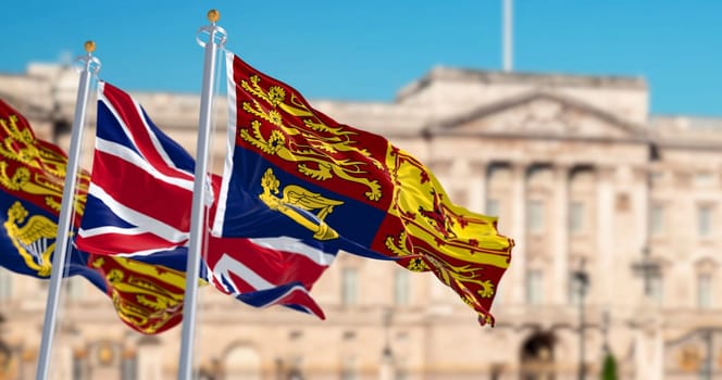 The Royal Standard of the United Kingdom waving with the UK flag with blurred Buckingham Palace in the background. 3d illustration render. rippled textile
