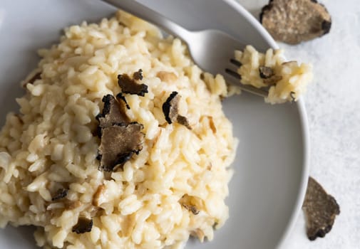 Risotto with wild porcini mushrooms and black truffles from Italy served in a plate top view on white table. Eating Italian gourmet cousine