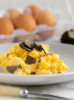 Scrambled eggs with sliced fresh black truffles from Italy served in a plate near fork and knife close up. Italian cousine, gourmet breakfast