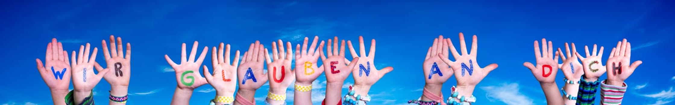 Children Hands Building Colorful German Word Wir Glauben An Euch Means We Believe In You. Blue Sky As Background.