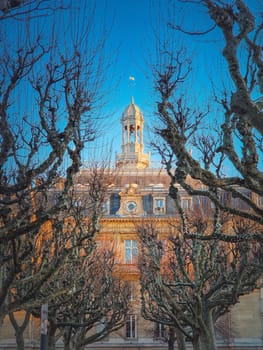City Hall of Asnieres as seen through the sycamore trees alley outdoors in the park. Asnières-sur-Seine mairie backyard facade view, northwestern suburb of Paris, France