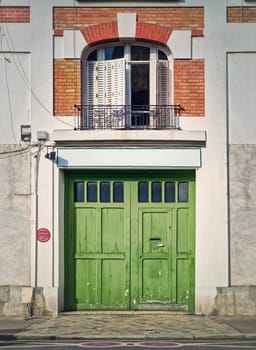 Town building facade with a green garage gate and window with louvers above the door