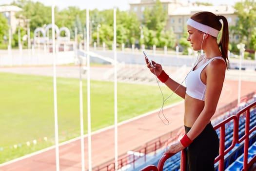 Sporty girl with earphones and iphone visiting stadium