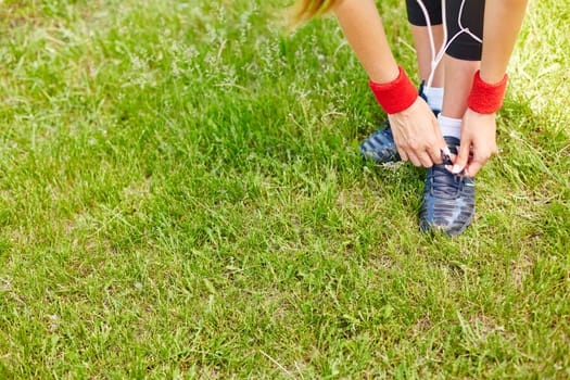 Sporty girl tying shoelaces of her sneakers while standing on grass