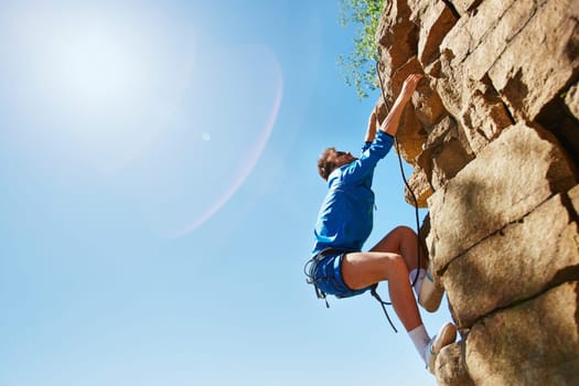 Young man climbing on top of rocky mount