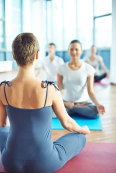 Back of sport trainer showing meditation exercise to young people
