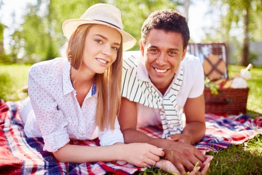Happy young couple looking at camera while relaxing in park
