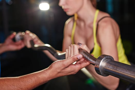 Hand of trainer helping young woman lift weight