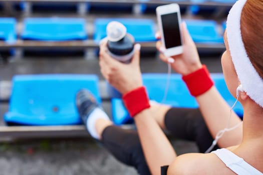 Modern girl with earphones and iphone sitting at stadium