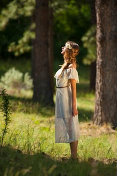 Vertical photo of beautiful young boho woman standing in forest with dramatic sunlight