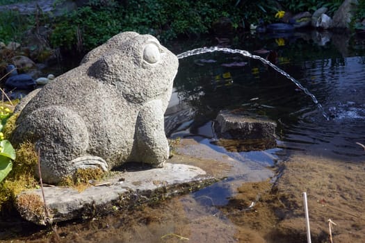 Wasser speiender Frosch aus Stein an einem Gartenteich