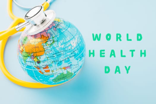 World Health Day Concept. Top view yellow doctor stethoscope and world globe isolated on pastel blue background with copy space, Save world day, Environment Green Earth, Health care and medical