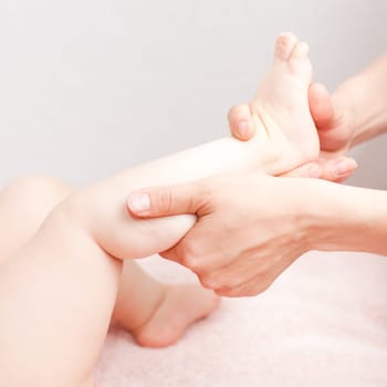 Masseuse massaging little baby girl's foot, shallow focus