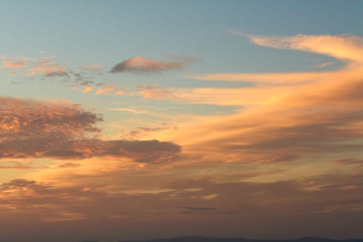 A picturesque sunset scene with clouds scattered across the sky, reflecting warm hues of orange and yellow over a body of water. Perfect for themes of nature's beauty and tranquility.
