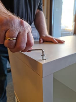 Detail from male Hand screwing a white shelf together