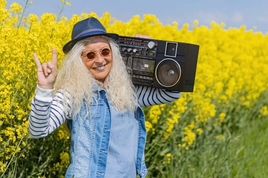 Elderly Woman have fun and shows metal sign with vintage Boom Box in Nature.