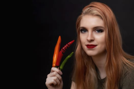 Attractive young woman with red lips is posing with  multicolored chili peppers. One paprika has the inscription paprika carved into it.