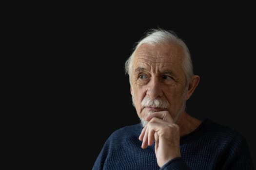 Beautiful gray hair old man wirh wrinkled face is posing on black background peeking to the right. Horizontally.
