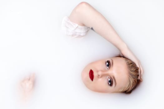 Young girl with red lips is lying  in spa bath with milk looking at the camera.  Horizontally.