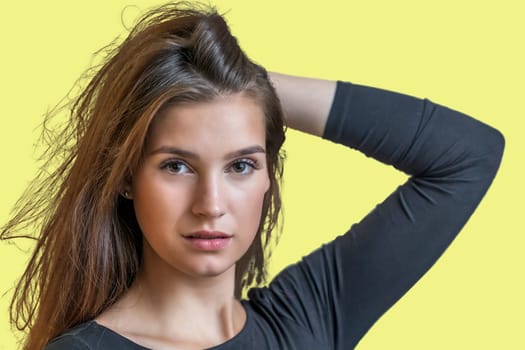 Portrait of beautiful long haired girl posing on yellow  background.  Horizontally.