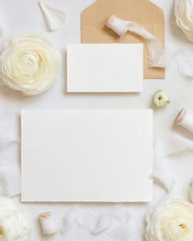 Blank cards near cream roses and white silk ribbons top view, wedding mockup. Romantic scene with horizontal cards and pastel flowers flat lay. Valentines, Spring or Mothers day concept