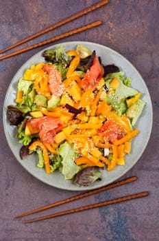 Fresh salad with salmon, mango, sesame and vegetables. Salad and chopsticks