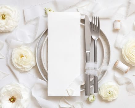 Wedding table setting with card near cream roses and white silk ribbons top view, mockup. Romantic scene with vertical menu card and pastel flowers. Valentines, Spring or Mothers day concept