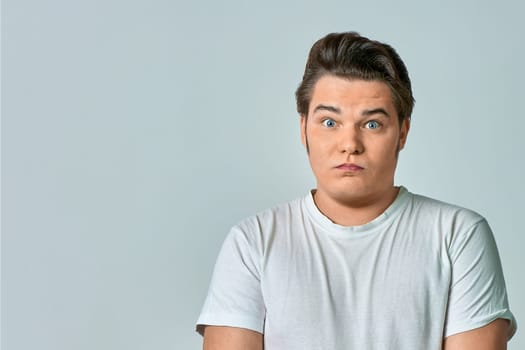 a surprised man on a gray background in a white T-shirt, copy space. High quality photo