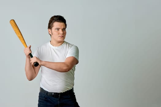 A man with a bat in his hands swings on a gray background. High quality photo