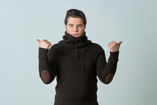 A man in a brown sweater on a gray background raised his hands. High quality photo
