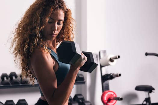 strong sportswoman doing exercise on biceps with dumbbells during workout at gym, concept of fitness and active lifestyle, copyspace for text