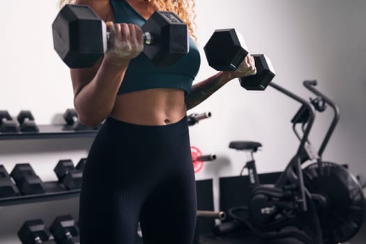 crop of unrecognizable strong sportswoman doing exercise on biceps with dumbbells during workout at gym, concept of fitness and active lifestyle