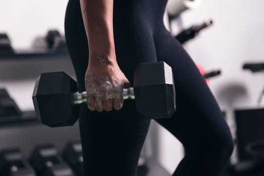 Detail of the hand of an unrecognizable strong sportswoman doing exercise with dumbbell during workout in gym, concept of fitness and active lifestyle